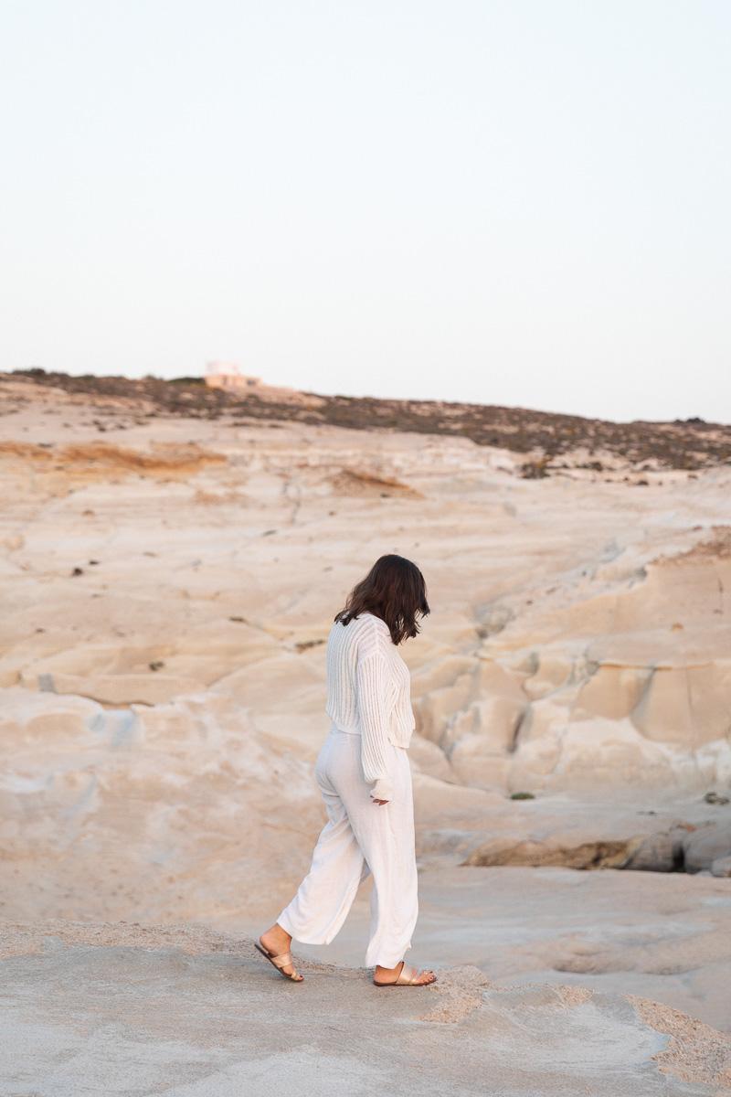 A woman in white walking across pale volcanic rock in Milos