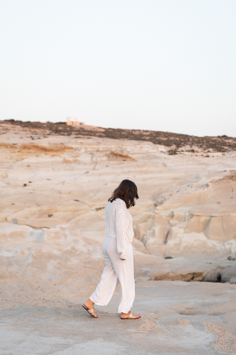 A woman in white walking across pale volcanic rock in Milos